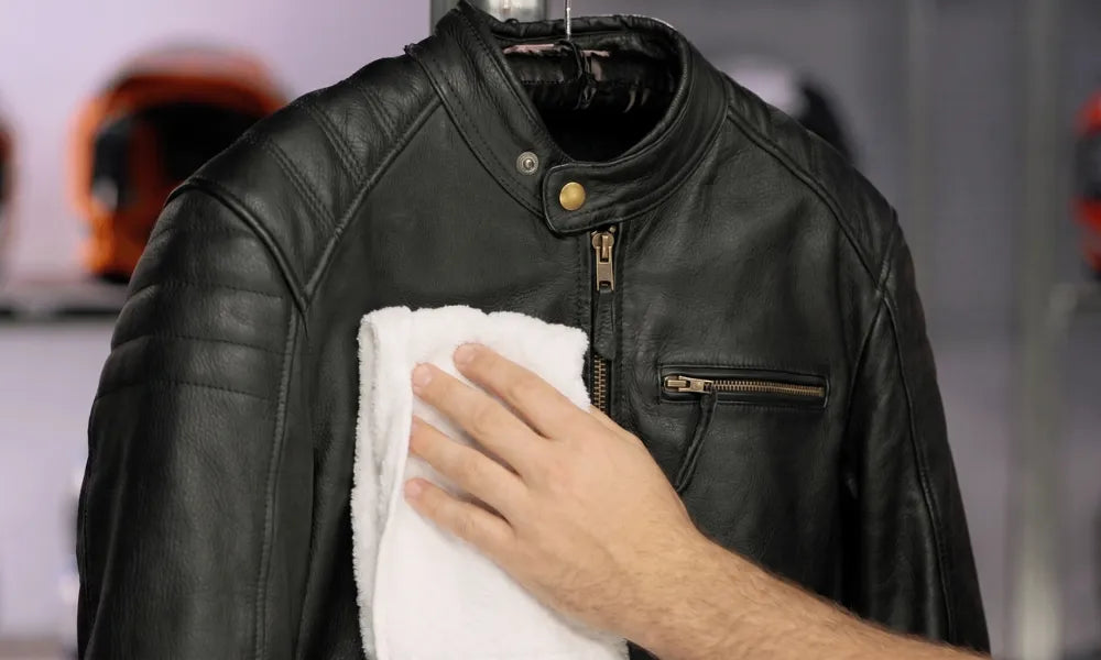 Cleaning a leather jacket with a microfiber cloth as part of a step-by-step leather care routine at home.