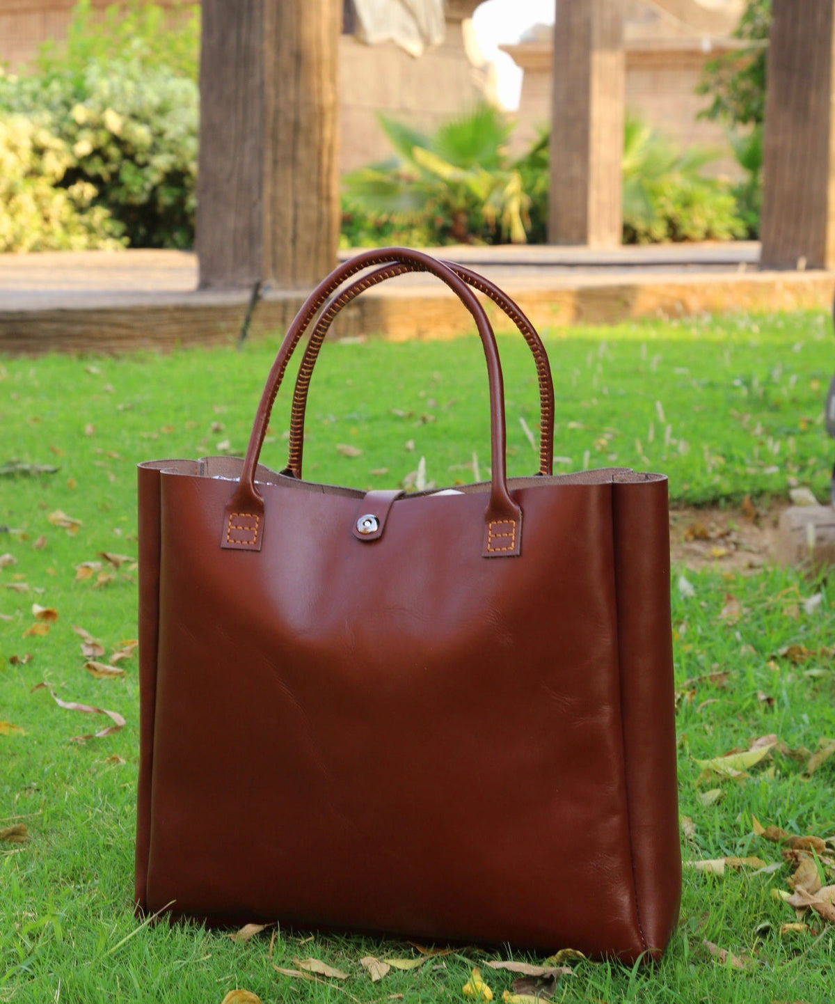 Brown leather tote bag on grass with architectural background