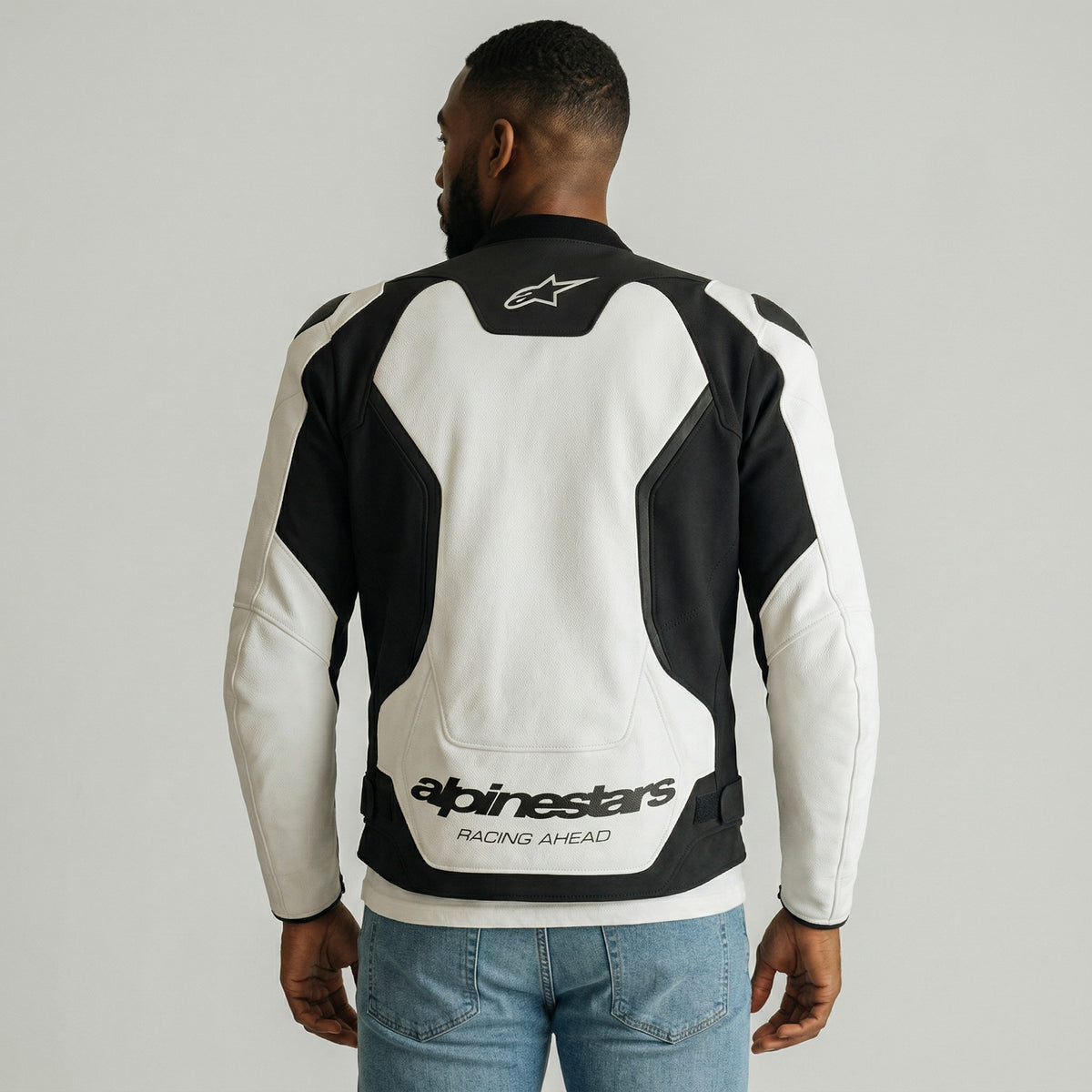 Person wearing a black and white alpinestars gp force motorcycle jacket with Alpinestars branding on a gray background