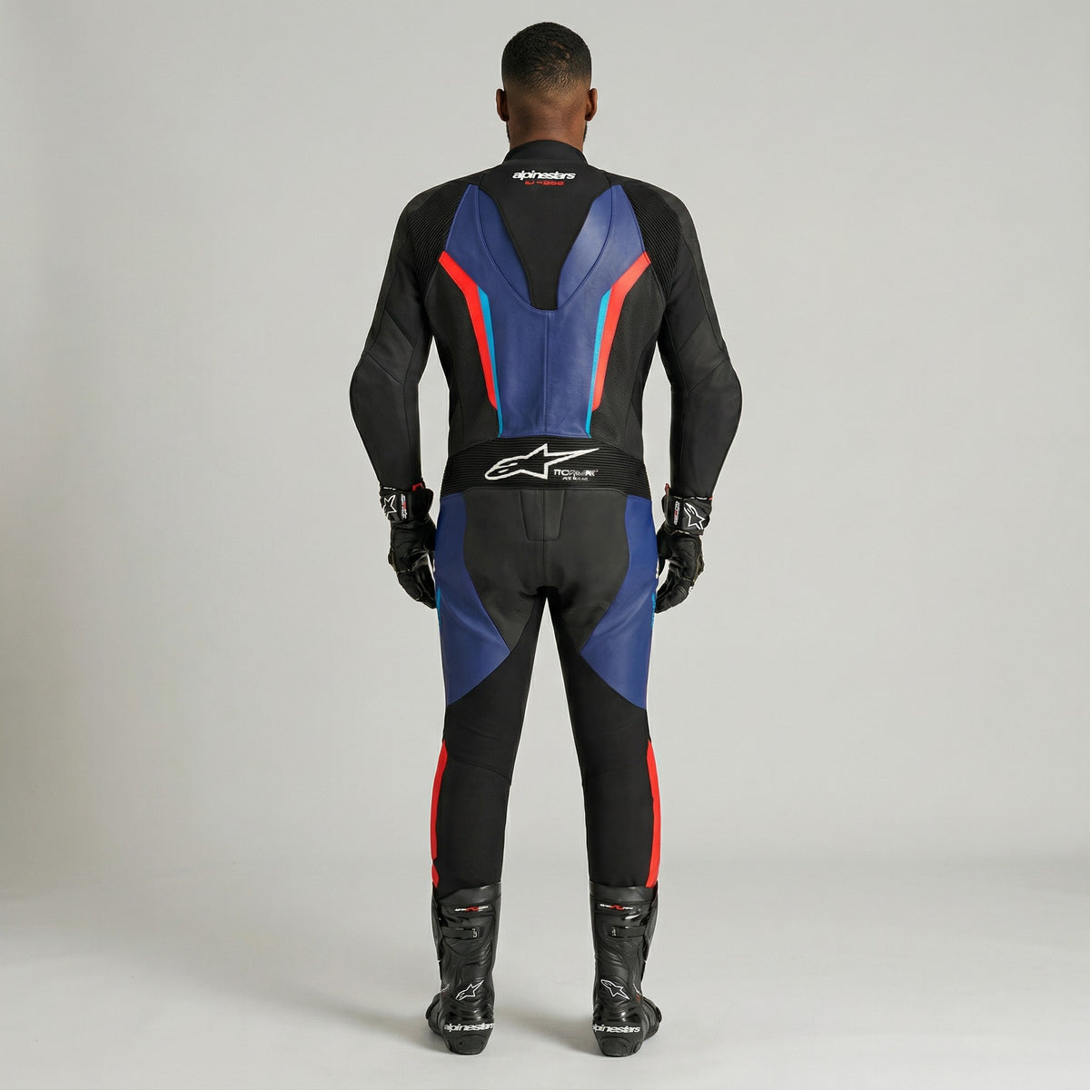 Person wearing a black, blue, and red motorcycle suit on a gray background