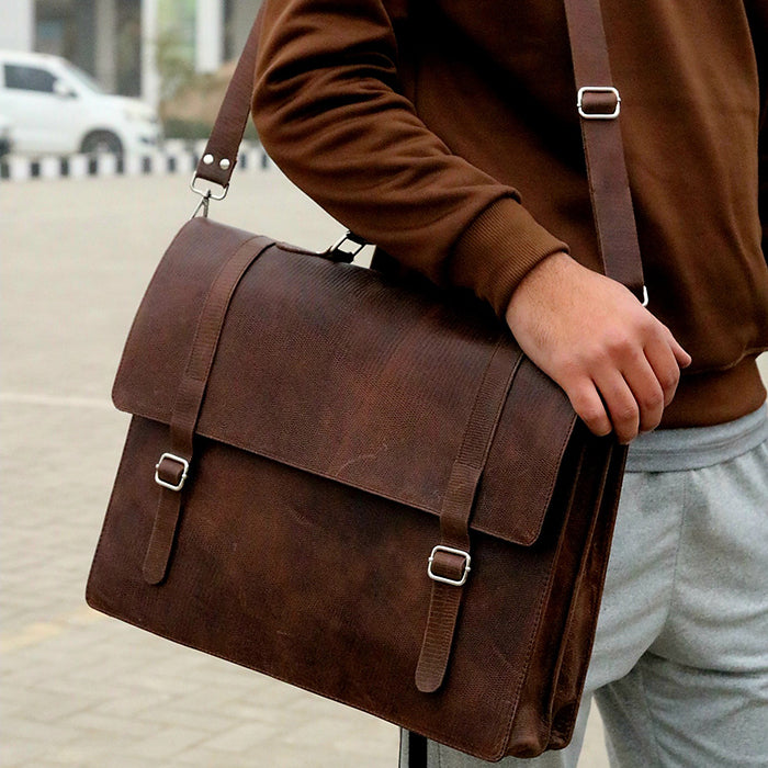 A person carrying a brown leather laptop bag with brass hardware and a shoulder strap.