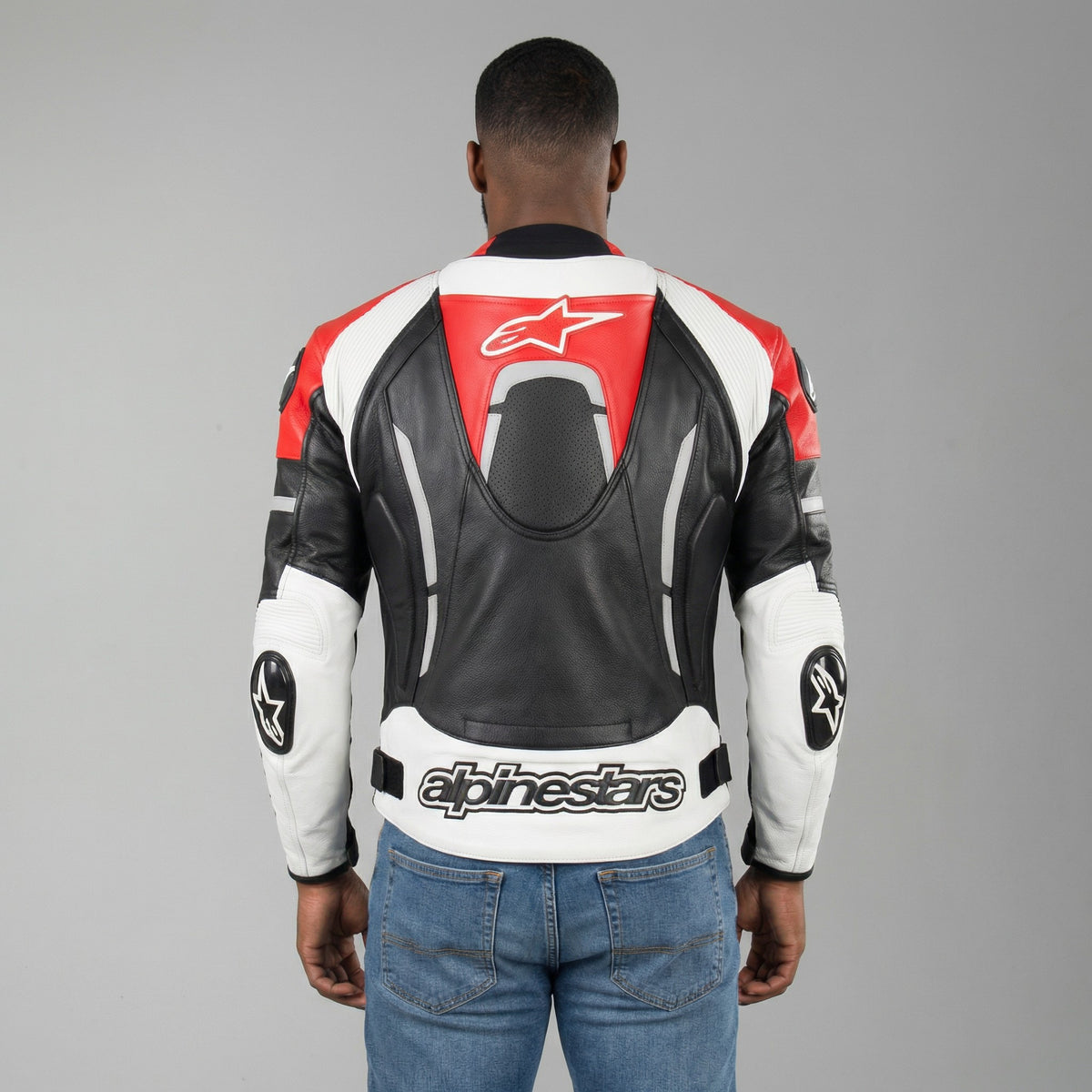 Person wearing a black, red, and white Alpinestars leather jacket on a gray background