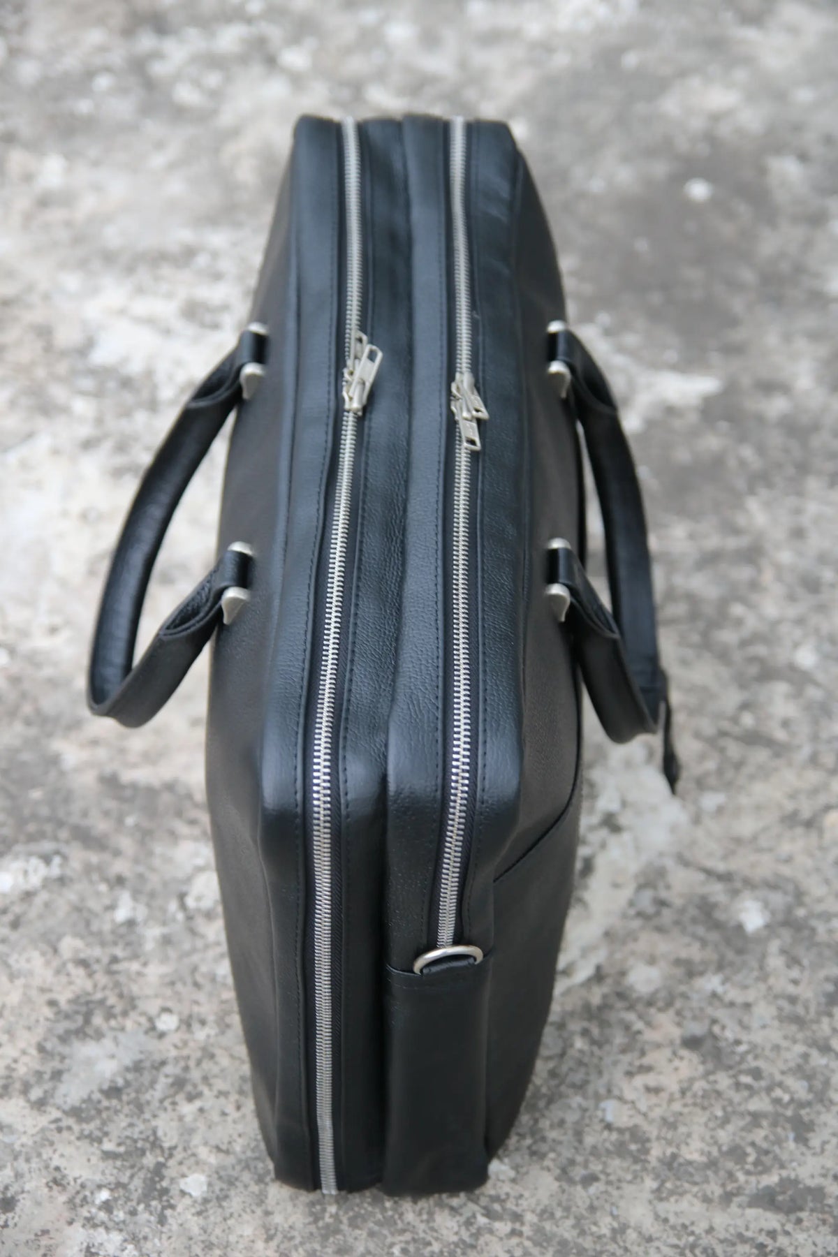 Black leather briefcase with zippers on a gray concrete surface