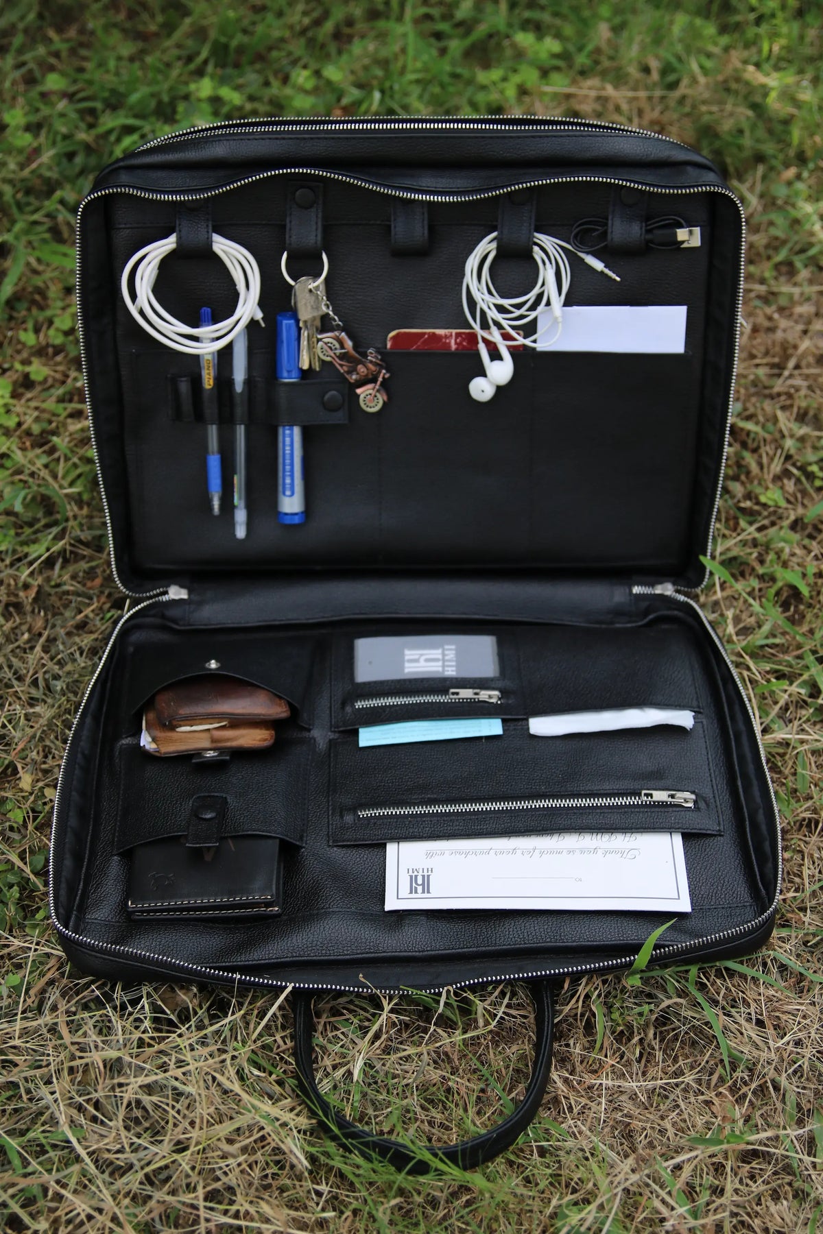 Black leather travel organizer with various items on a grassy background