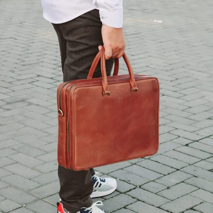 Person holding a brown leather briefcase on a paved ground