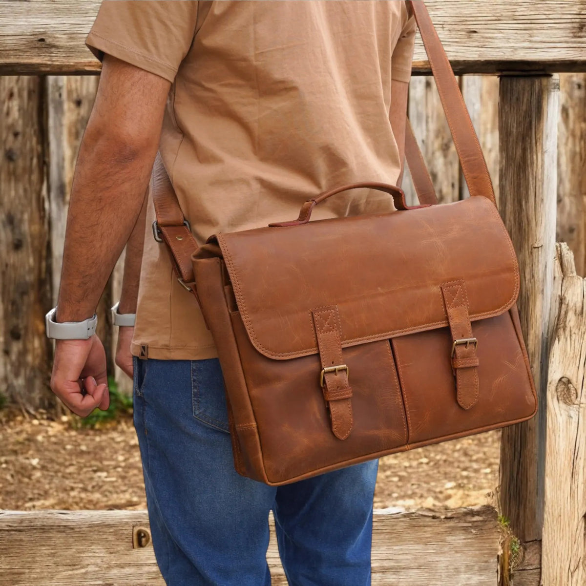 Person wearing a brown leather messenger bag outdoors.