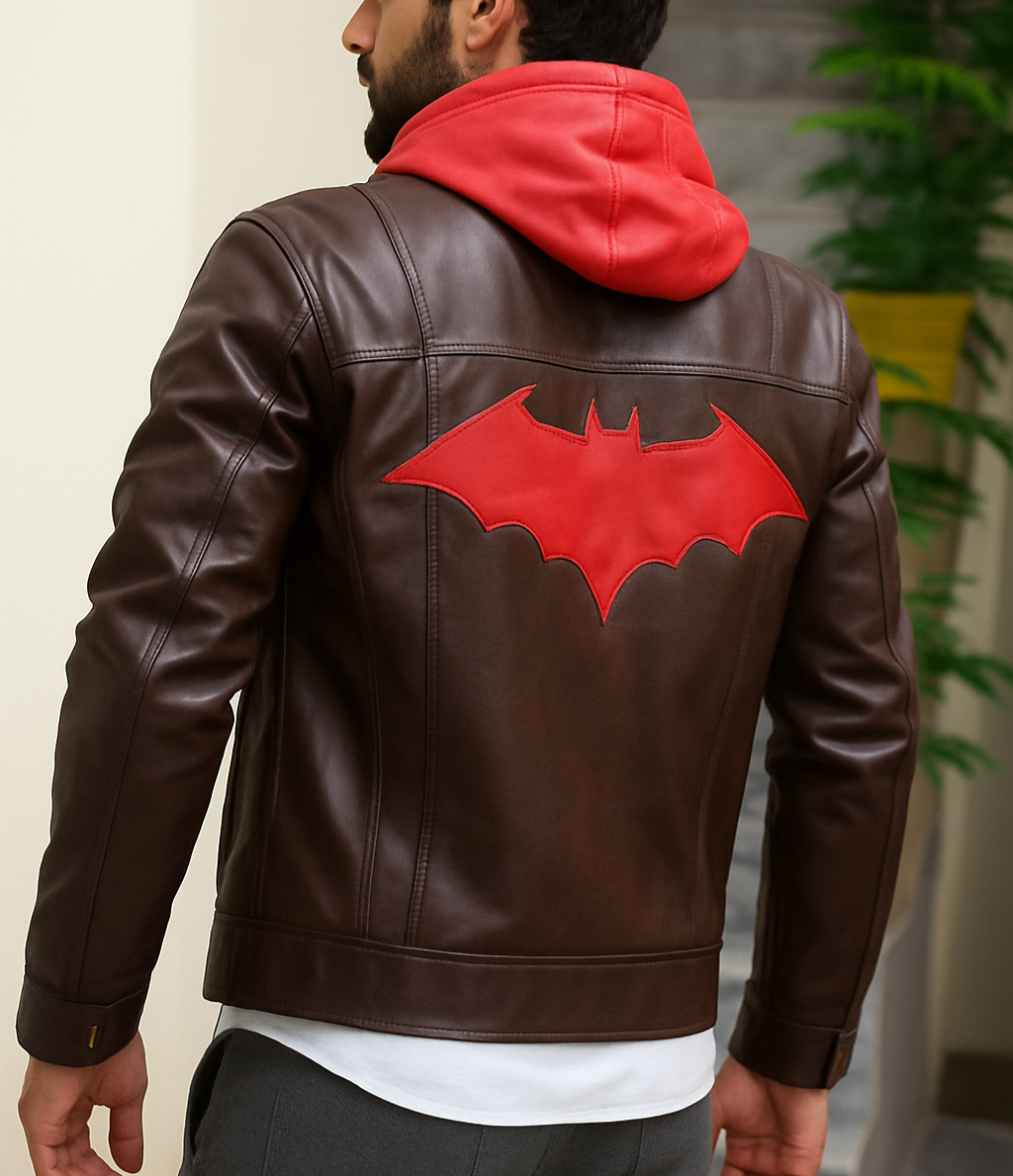 Man wearing a brown leather jacket with a red bat symbol on the back, standing indoors.