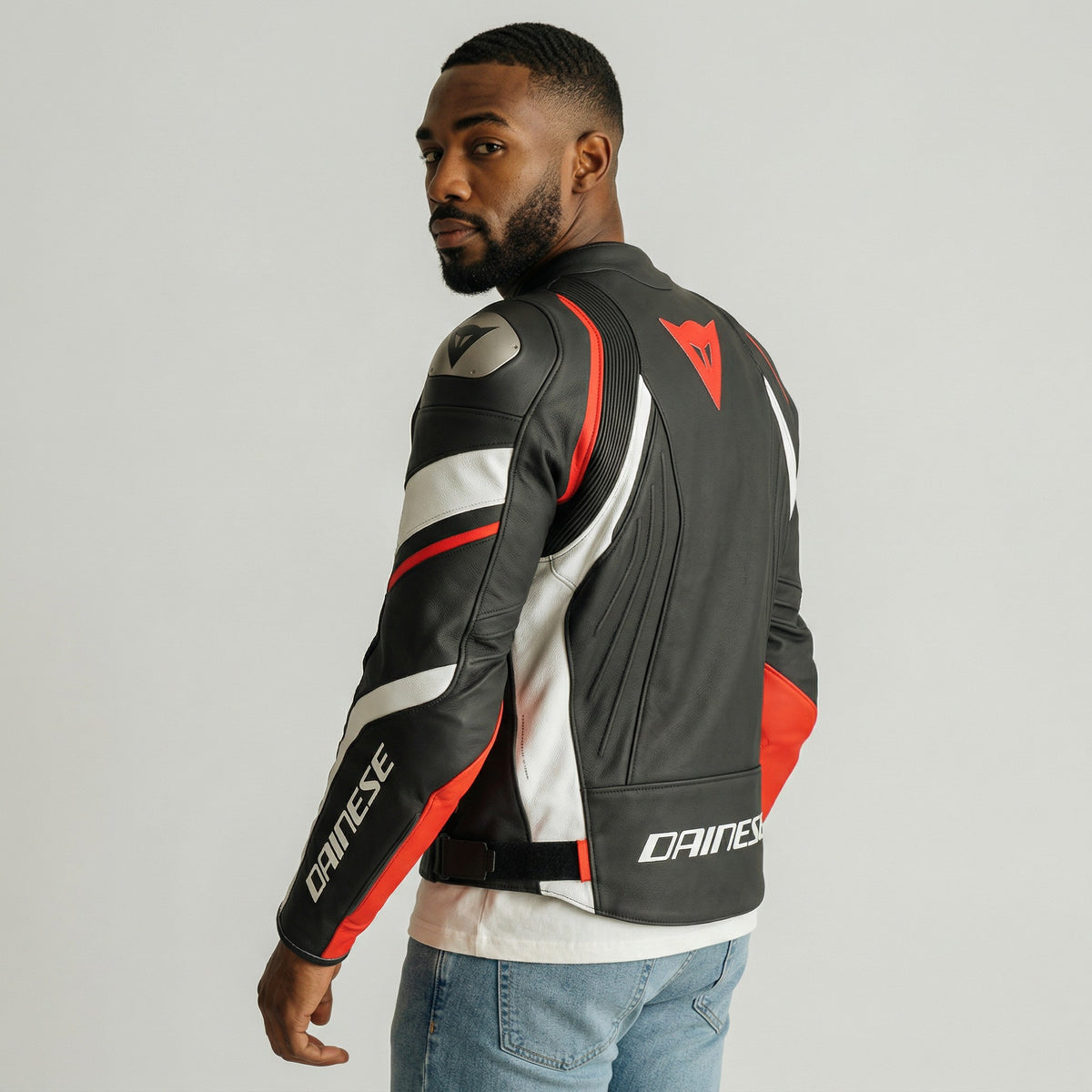 Man wearing a black, red, and white Dainese motorcycle jacket on a gray background