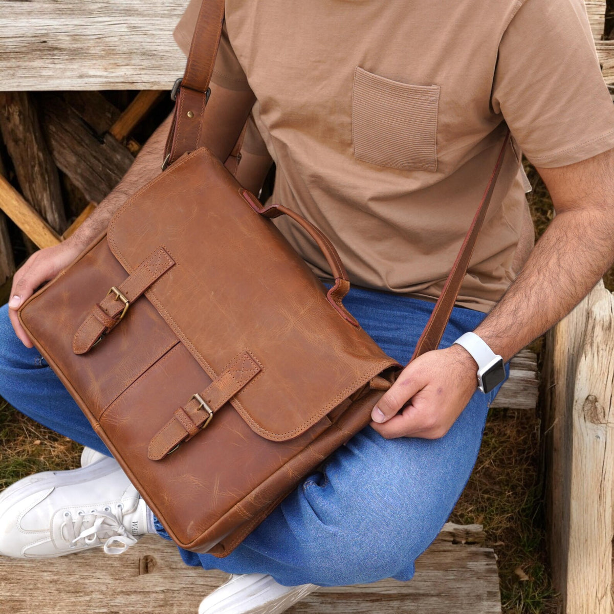 Person holding a brown leather messenger bag outdoors