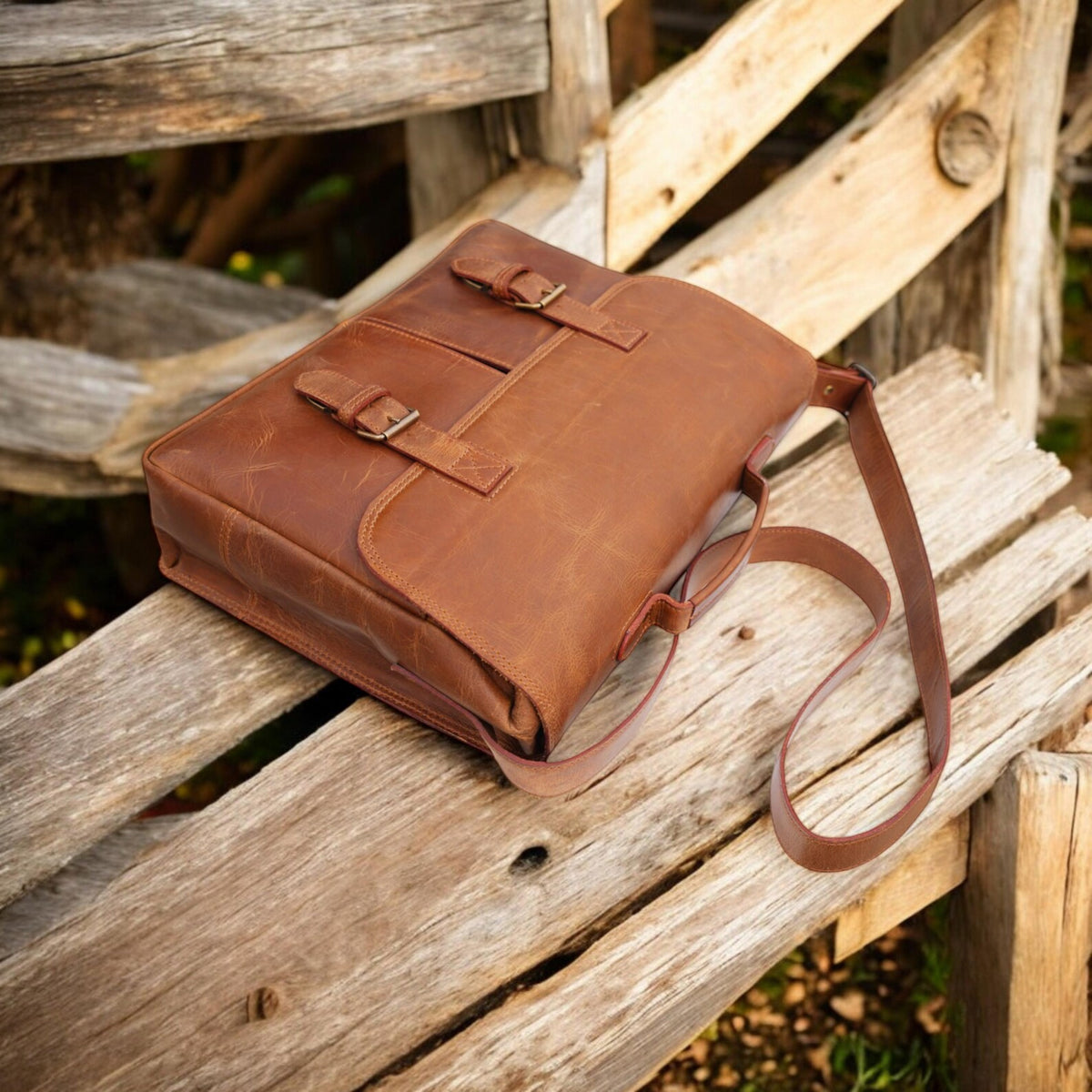 Brown leather messenger bag on a wooden bench